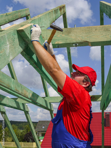Carpenter driving a nail into house rafter framing beam