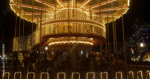 The illuminated carousel in the amusement park is spinning at night. The beautiful park is having fun