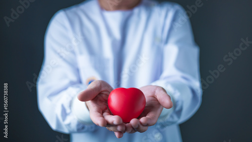 A healthcare professional in a white coat gently holds a red heart model in both hands, symbolizing cardiac care, heart health awareness, medical compassion, and support in cardiovascular wellness.