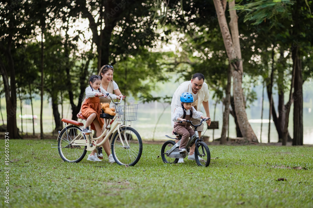 Obraz premium A family of four riding bikes in a park. A man is riding a bike with a child on it