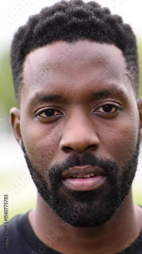 afro-american man with beard, short curly hair, serious expression looking directly at camera in close-up, head-on video with subtle movement and soft outdoor light serious portrait concept photo