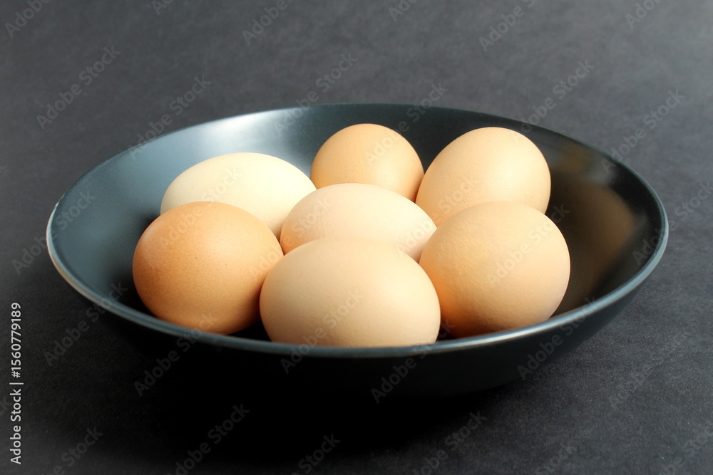 On a black background, there are chicken eggs in a black plate. On a black background, there are chicken eggs in a black plate.