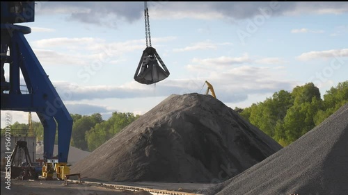 A port crane unloads crushed stone and other bulk materials from a bulk carrier in a river port