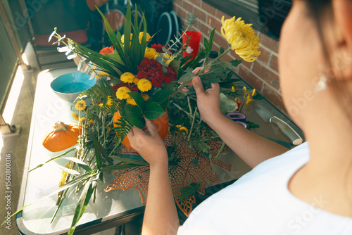 Woman preparing autumn centerpiece with flowers and pumpkin