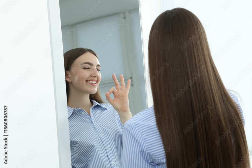 Fototapeta premium Beautiful woman showing ok gesture near mirror indoors