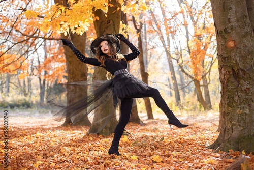Woman in witch costume standing in autumn forest on Halloween