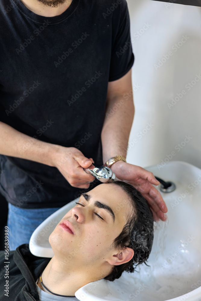 Fototapeta premium Teenager Getting Hair Washed at Modern Barbershop. Male Barber Washing Client’s Hair at Sink in Hair Salon. Teenager and haircut, Men's grooming and care, Hair care for guys, Teenage beauty