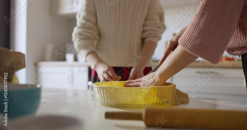 Close up of mother and daughter Place the dough in a mold and trimming knife while making pie in pan on cozy kitchen table
