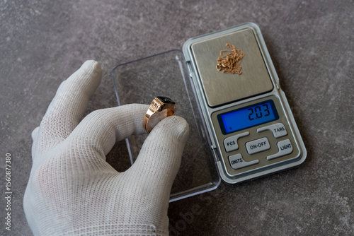 A white-gloved hand holds a gold ring.Estimating the value of jewelry in the store.