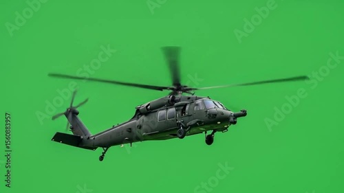 A black hawk helicopter with rotating blades flying against a solid bright green background in the sky