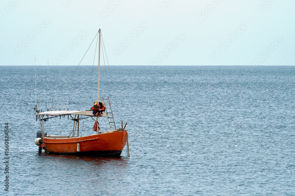 Fototapeta premium Sea fishing. A lonely red boat with many different fishing rods on board is anchored in the middle of the sea.