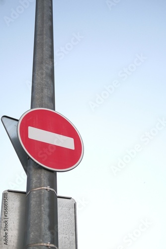Red no-entry traffic sign on metal pole, clear sky background. Do not enter round sign for cars, regulation on roads. Metaphor for stop doing something. Vertical backdrop with space for text