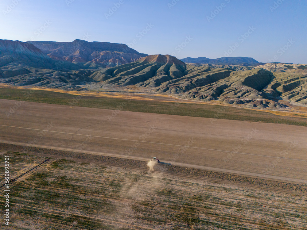 Obraz premium Nallıhan Aerial View of a Dusty Field with Dramatic Mountains. High-angle, expansive shot of a dry, flat field, likely farmland, with a light dusting of dust rising from a vehicle or machine traversin