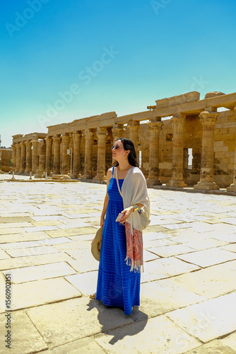 Woman in a blue dress with a white scarf holding a hat at the Philae Temple in Egypt
