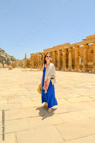 Woman in a blue dress with a white scarf holding a hat at the Philae Temple in Egypt