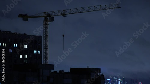 Silhouette of a construction site and tower crane at night against a modern city skyline with illuminated skyscrapers in the background. Urban development, infrastructure growth