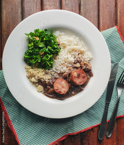 Brazilian food, with white plate with rice, feijoada, sautéed kale and farofa