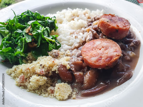 Brazilian food, with white plate with rice, feijoada, sautéed kale and farofa and blurred background