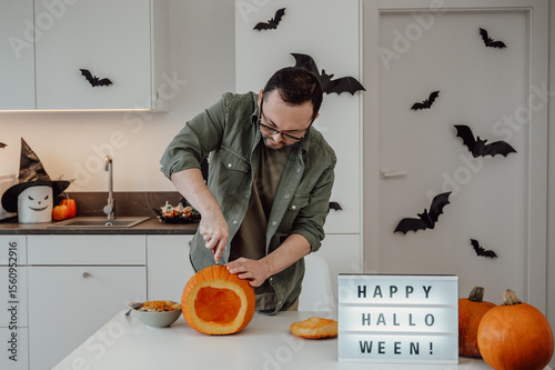 Halloween concept. Man in a decorated house carves halloween lantern from pumpkin. October 31 celebration