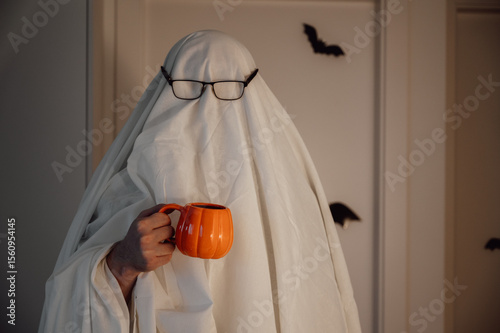 Person in costume of ghost hold pumpkin shaped cup.Halloween celebration banner with copy space. Spooky shot