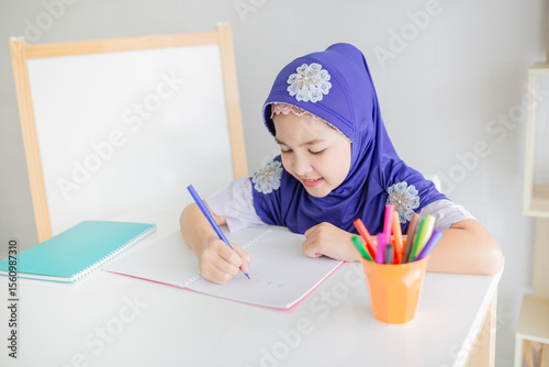 Happy Muslim girl in a purple hijab writing in her notebook at a white desk, with colorful pens beside her. Concept of education, creativity, and childhood development. she doing homework.
