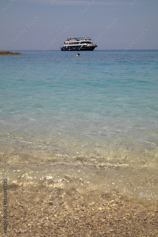 Obraz premium pebble beach and clear water with distant boat