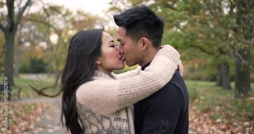 Romantic Asian couple shares a passionate kiss while embracing in a beautiful autumn park.