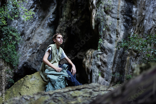 A hiker rests on a mossy rock inside a rocky canyon, surrounded by lush greenery. The peaceful scene captures a moment of solitude, reflection, and connection with nature during an outdoor adventure.