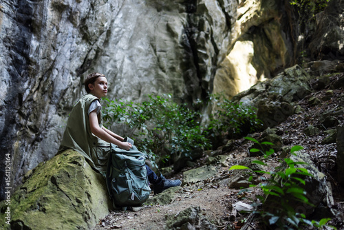A hiker rests on a mossy rock inside a rocky canyon, surrounded by lush greenery. The peaceful scene captures a moment of solitude, reflection, and connection with nature during an outdoor adventure.