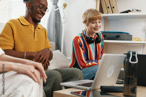 young adult coworkers socializing at workplace with laptop smiling woman and man collaborating in casual work environment with friends and business vibe