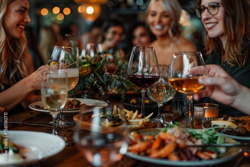 Four happy women in their 20s and 30s celebrate at a cozy restaurant dinner party. They enjoy wine glasses filled with red wine and delicious seafood appetizers, creating a warm and joyful atmosphere.