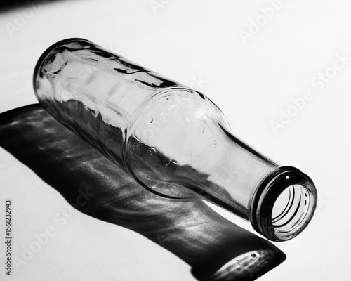 A clear glass bottle lies on its side casting a dramatic shadow in strong light