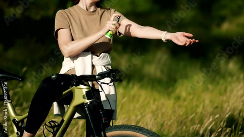woman spraying insect repellent on arm outdoors near bicycle