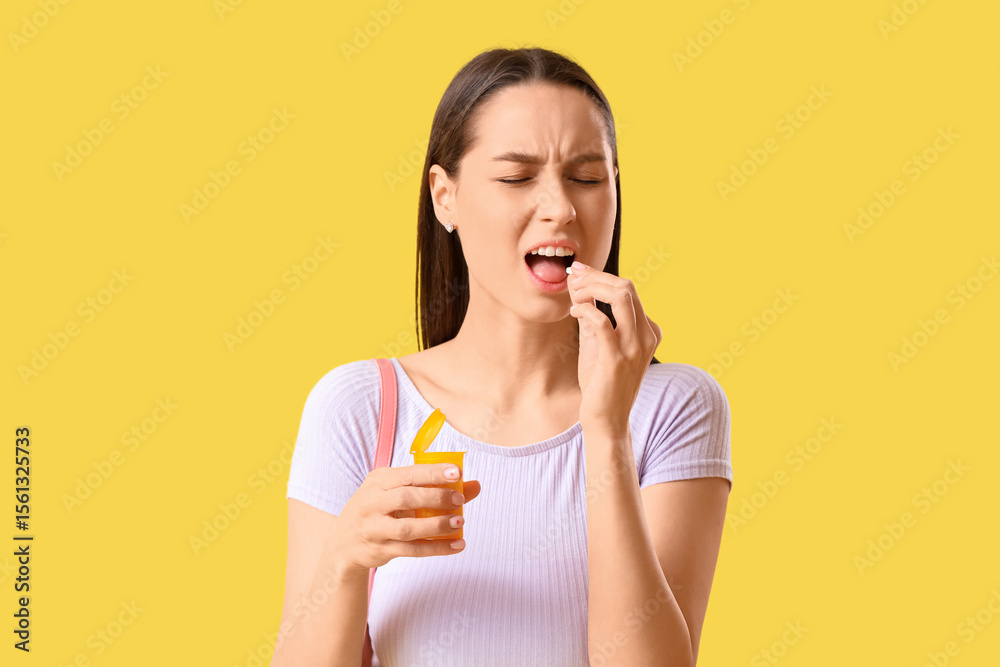 Young woman with pills for sore throat on yellow background