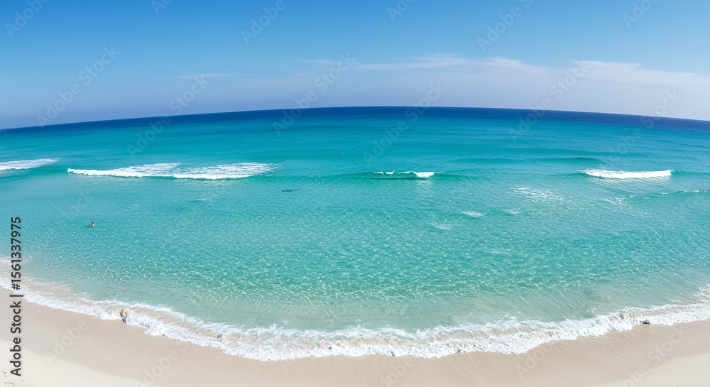 Fototapeta premium Bright turquoise ocean waves gently crashing onto white sandy beach under clear blue sky with distant horizon and calm sea surface