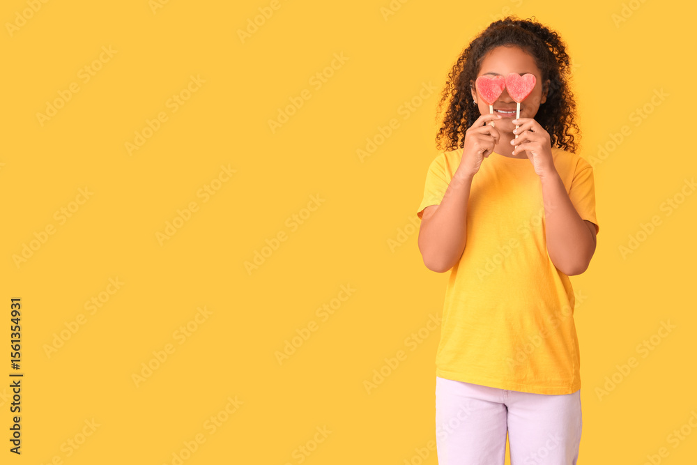 Cute African-American girl holding sticks with sweet watermelon in shape of hearts on yellow background Cute African-American girl holding sticks with sweet watermelon in shape of hearts on yellow background