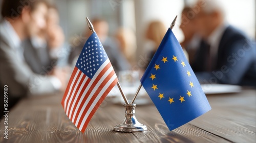 Close-up of USA and European Union flags crossed on a meeting table, symbolizing international relations, diplomacy, and cooperation. Blurred business professionals in the.