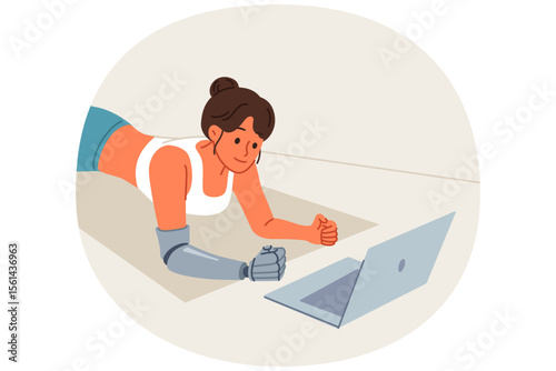 Sports woman with prosthetic arm trains at home and watches video lesson on laptop, lying on floor in plank. Sports girl doing yoga on fitness mat, training to improve health and muscle development