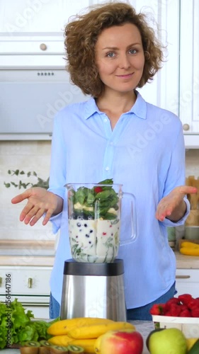 Vertical screen happy woman adding ingredients to a blender in her kitchen, preparing a healthy and refreshing smoothie with various fruits and vegetables
