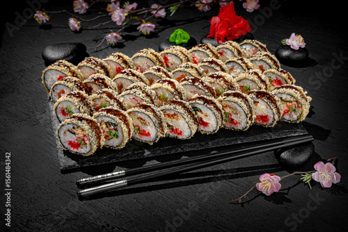 Sushi set tempura beautifully arranged on a textured black surface with a blooming cherry blossom branch in the background. Traditional Japanese elegance meets modern food styling.