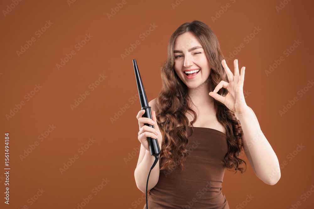 Obraz premium Woman curling her beautiful hair on brown background. Space for text
