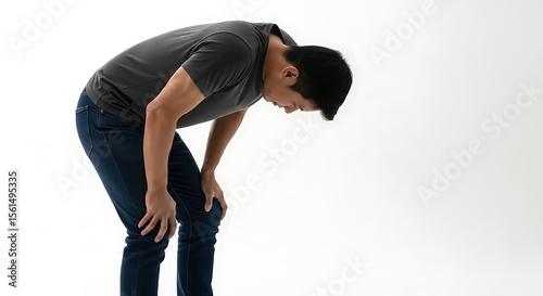Man in gray shirt and jeans bending over with hands on knees against white wall