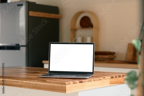 Laptop on a clean countertop with a refrigerator and kitchen decor in the background