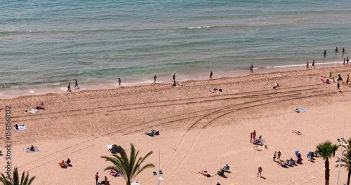 Slow motion aerial footage of the lively Spanish city of Benidorm showing the Playa de Levante beach with local people and tourists on vacation relaxing sunbathing enjoying the sandy beach