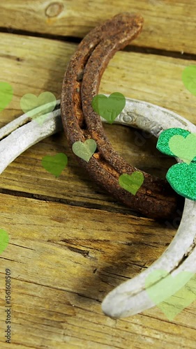 Animation of st patrick's shamrock, horseshoe and green hearts on wooden background