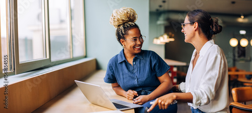 Cuadro en lienzo Two young women smiling and talking while working together at a laptop