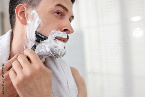 Fototapeta Handsome man shaving with razor at home. Space for text