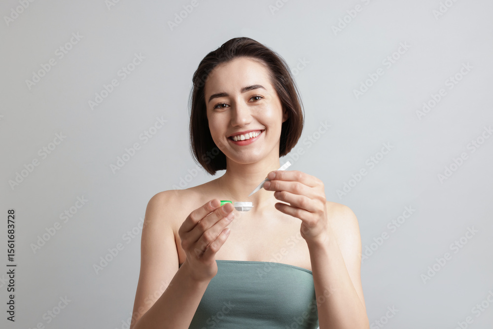 Woman taking contact lens out of case on light background