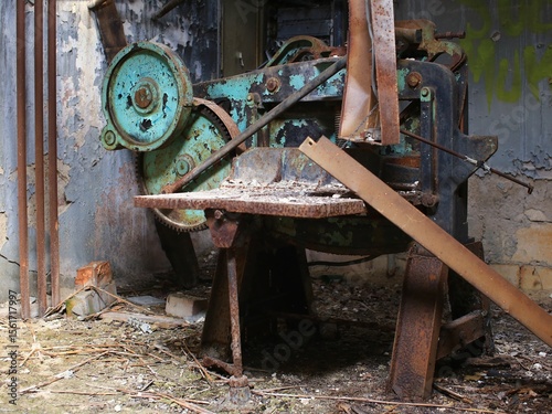 Rusted industrial machine in abandoned workshop surrounded by debris and peeling paint