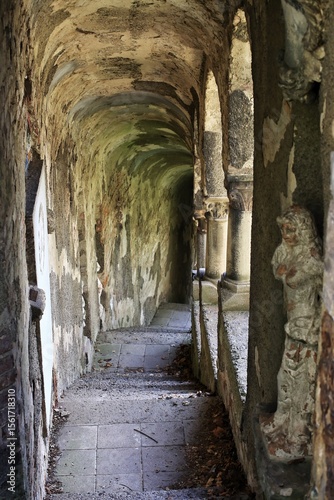Weathered stone corridor lined with statues and flaking walls in dim, narrow passageway